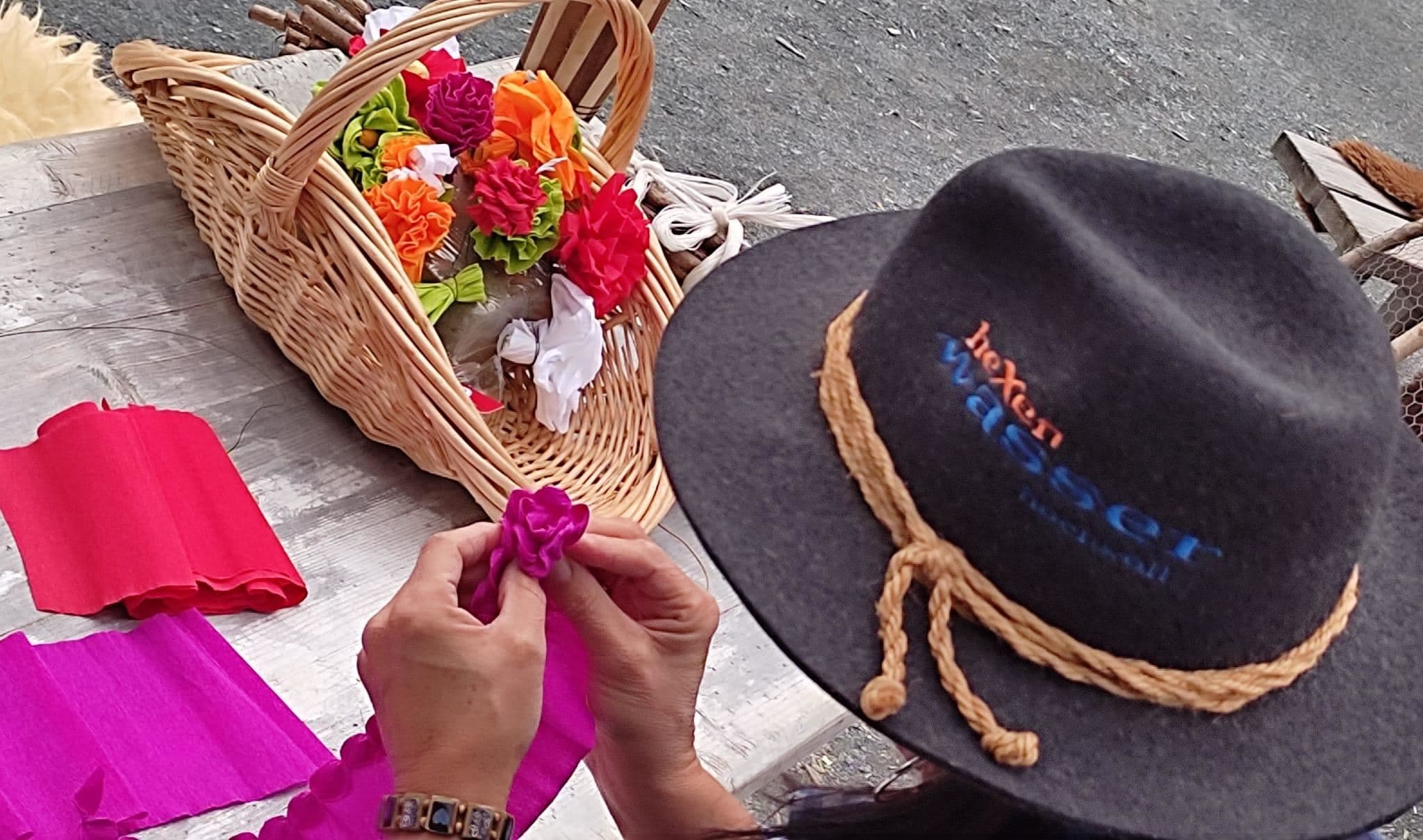 A person is crafting flowers out of colorful fabric. In the background, there is a basket with already completed flowers.