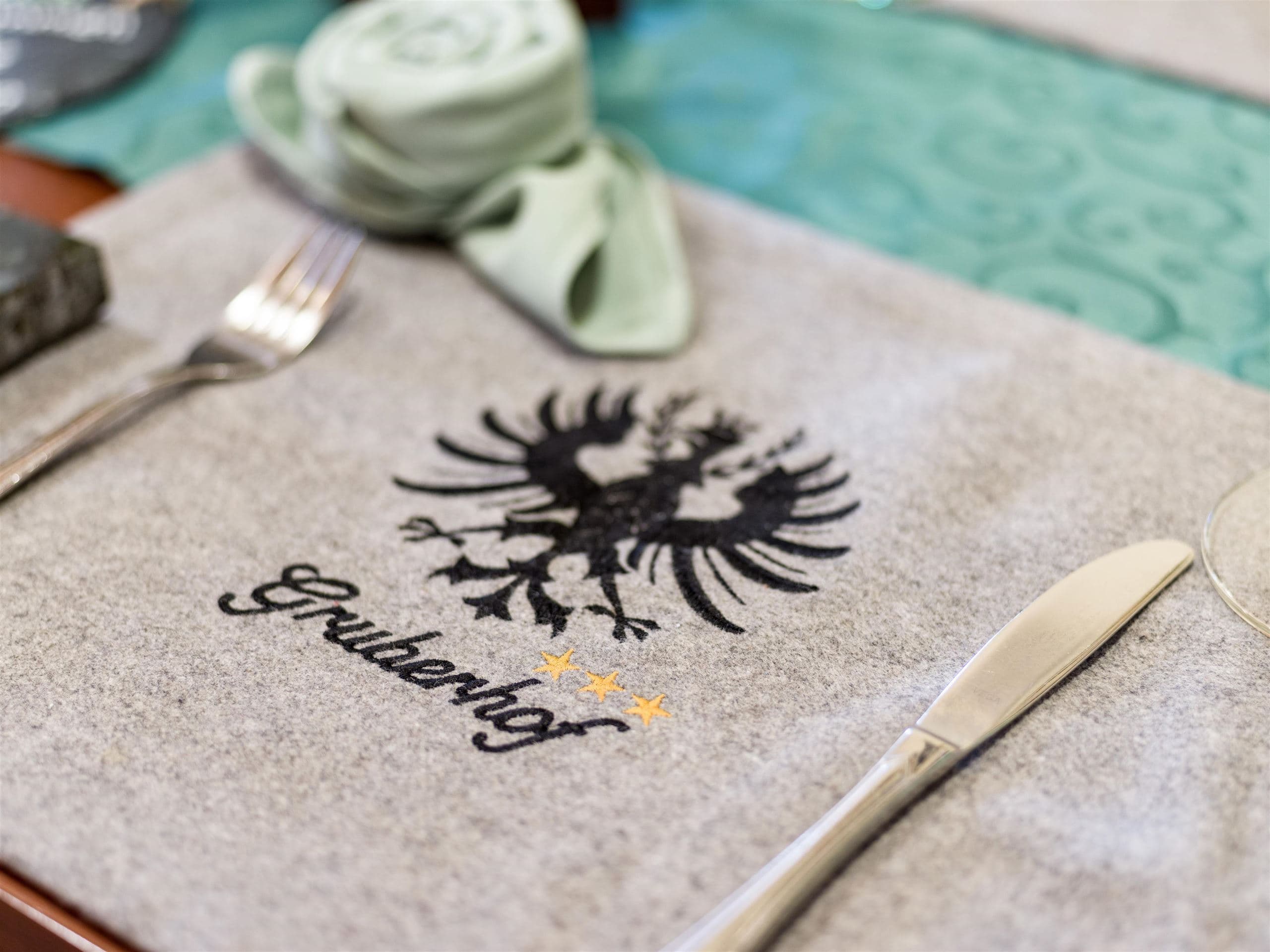 An elegant tablecloth featuring the coat of arms and the name "Grudenhof." The design is simple and inviting, with cutlery neatly arranged.